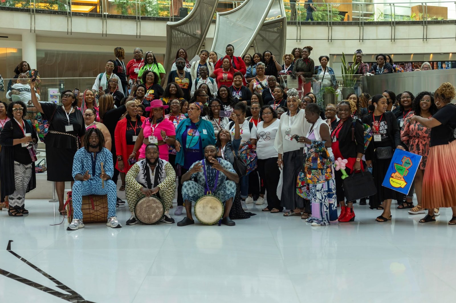 Large group photo of attendees and drummers in a convention hall.