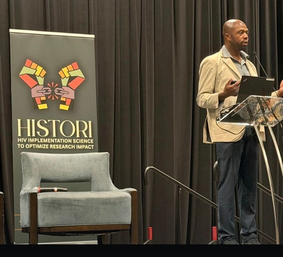 A speaker at the NAESM conference beside a HISTORI banner.